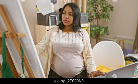 Junge schwangere Künstlerin, die in ihrer Konzentration auf ihrem Laptop in ihrem Atelier zeichnet Stockfoto