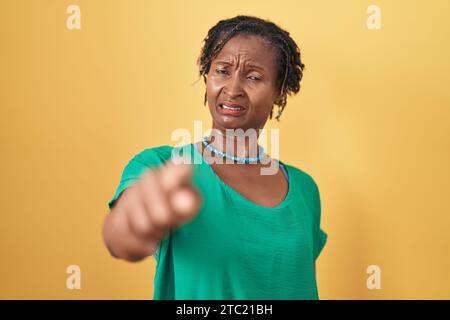 Afrikanische Frau mit Dreadlocks, die über gelbem Hintergrund steht und unzufrieden und frustriert auf die Kamera zeigt, wütend und wütend auf dich Stockfoto