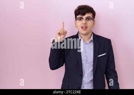 Junger, nicht binärer Mann mit Bart, Anzug und Zeigefinger mit gelungener Idee. Verlassen und glücklich. Nummer eins. Stockfoto
