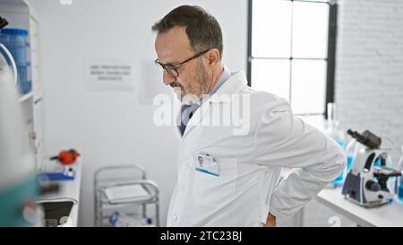 Mittelalter grauhaariger Wissenschaftler, der Rückenschmerzen hat und sich um das Pressen von Laborarbeiten am Computer bemüht Stockfoto