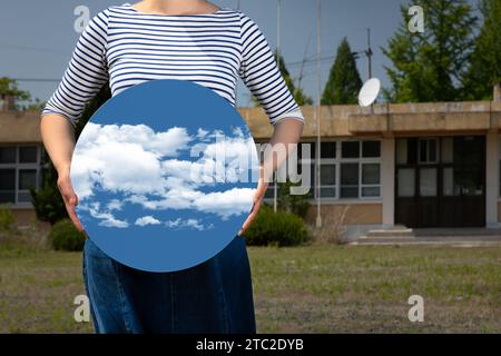 Surrealismus mit einer Frau, die einen Spiegel hält und ihr Gesicht vor einer alten Schule bedeckt, mit einem transparenten Hintergrund hinter dem Spiegel Stockfoto