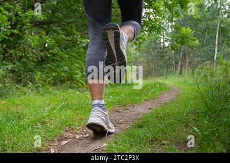 Die Füße einer Frau, die auf einem unbefestigten Pfad im Park im Grünen läuft Stockfoto