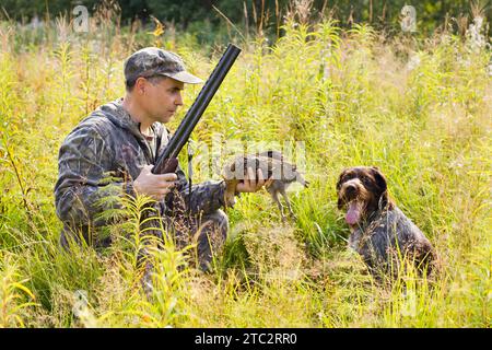 Der Jäger hält in der Hand ein abgestürztes Auerhühl, das von seinem Hund während der Jagd mitgebracht wurde Stockfoto