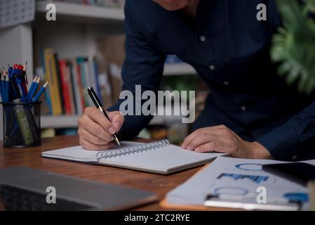 Ein Mann schreibt mit einem Stift auf einem Notizbuch im Büro. Lernen, Bildung und Arbeit. Schreibt Ziele, Pläne, To-do und Wunschliste auf dem Schreibtisch. Stockfoto