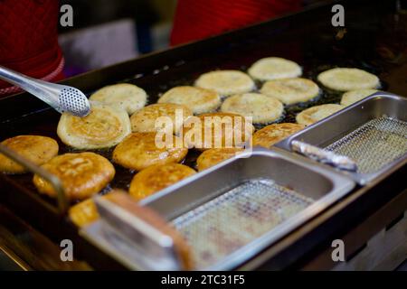 Ein Verkäufer frittiert geschickt Hotteok, ein beliebtes koreanisches Street Food, auf einem traditionellen Markt und erfüllt die Luft mit dem Aroma dieser köstlichen gefüllten Pfanne Stockfoto