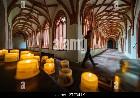 Mainz, Deutschland. Dezember 2023. Ein Besucher der St.. Stephans Pfarrkirche geht an Opferkerzen im Kreuzgang vorbei. Die katholische Pfarrkirche St. Stephen wurde 990 auf dem höchsten Punkt der Stadt gegründet. Der Kreuzgang mit seinem Rippengewölbe gilt als der schönste spätgotische Kreuzgang in Rheinland-Pfalz. Darlegung: Andreas Arnold/dpa/Alamy Live News Stockfoto