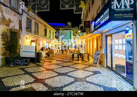 Eine farbenfrohe Straße mit Geschäften und Cafés mit Calcada-Pflaster in der Nacht, in der Altstadt des Badeorts Cascais Portugal. Stockfoto