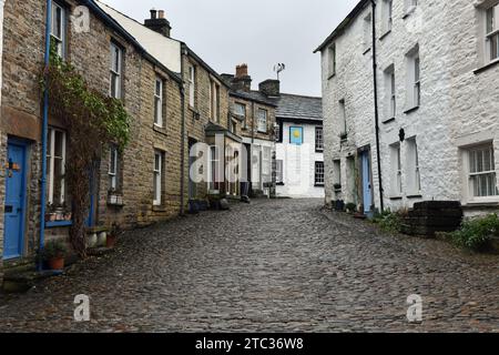 Die kopfsteingepflasterte Hauptstraße durch Dent Village in Dentdale - in der Ferne ist das Sun Inn mit gepflasterten Straßen und alten Häusern im Zentrum Stockfoto