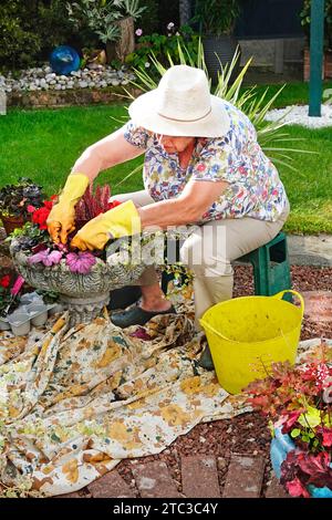 Reife ältere Frau mit Arthritis sitzend, Frühlingszwiebeln in Stein Pflanzgefäß recycelter Vorhang als Staubtuch Sonnenhut & Handschuhe England Großbritannien Stockfoto