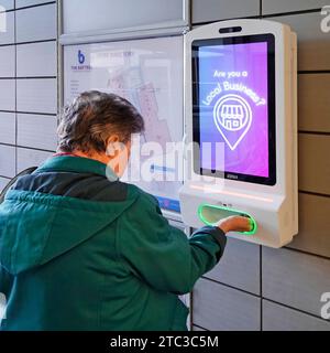 Ältere reife Frau Rückansicht steckt eine Hand in Schlitz an der Wand montierte automatische Desinfektionsgel Dispenser Bildschirm zeigt Werbung Einkaufszentrum Essex England Großbritannien Stockfoto