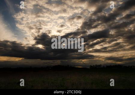 Sonnenuntergang über den Feldern der polnischen Landschaft kündigen tief fließende Wolken den kommenden Sturm an. Stockfoto