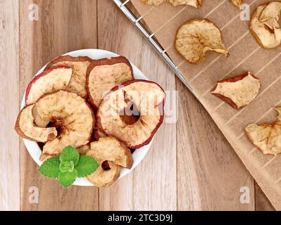 Getrocknete Apfelringe in weißer Schüssel auf einem Holztisch, hausgemachte Apfelringe auf einem Backblech aus dem Ofen Stockfoto