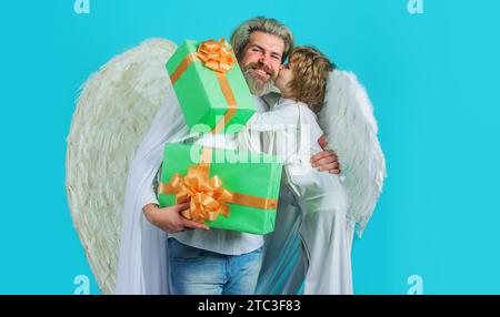 Valentines Engel Vater und Sohn in weißen Flügeln mit Geschenkbox. Kleiner Cupid Junge und lächelnder bärtiger Mann im Engelskostüm mit Valentinsgeschenken Stockfoto