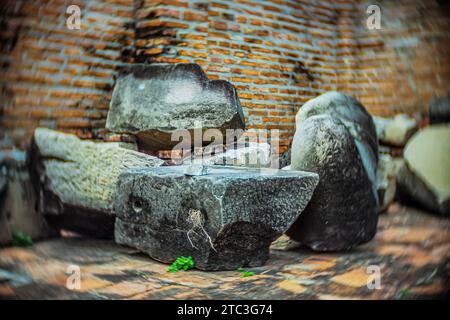 Verwitterte archäologische Steinfragmente und gebrochene Artefakte ruhen auf dem Boden neben einer alten verwitterten Tempelmauer in Thailand. Stockfoto