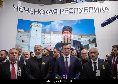 Moskau, Russland. Dezember 2023. Der Abgeordnete Adam Delimchanow, Russlands Stellvertretender Premierminister Alexander Novak und der Premierminister der Tschetschenischen Republik Muslim Huchiev (L-R-Front) sprechen bei der Eröffnung des Tages der Republik Tschetschenien während der internationalen Ausstellung und des Forums der russischen Expo im VDNKh-Ausstellungszentrum in Moskau, Russland, mit den Medien. Auf dem Banner steht "Tschetschenische Republik". Quelle: Nikolay Vinokurov/Alamy Live News Stockfoto