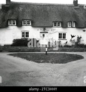 1960er Jahre, historisches, vorderes Äußere des Brace of Fasans, ein reetgedecktes Wirtshaus aus dem 16. Jahrhundert, in Dorset, England, Großbritannien. Über der Tür steht, dass der Pub ein Freihaus ist, nicht an eine Brauerei gebunden, mit dem Lizenzgeber Alfred Henry Elven. Auf dem Straßenschild steht: Piddletrenthide und Dorchester. Name über Tür, Lizenzgeber Stockfoto