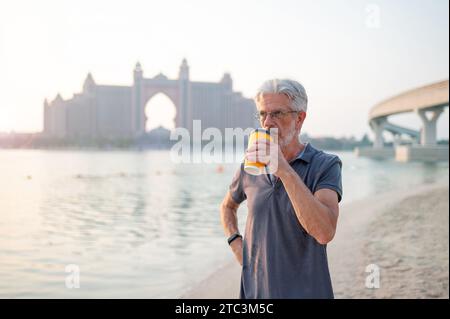 Senior kaukasischer Mann bei einer Tasse Kaffee und genießen die Schönheit von Palm Jumeirah in Dubai, gefangen vor der atemberaubenden Kulisse eines Sonnenuntergangs Stockfoto