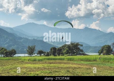 Gleitschirmflieger, der über die Wiese fliegt, Pokhara-Region, Nepal. Himalaya-Berge im Hintergrund. Stockfoto