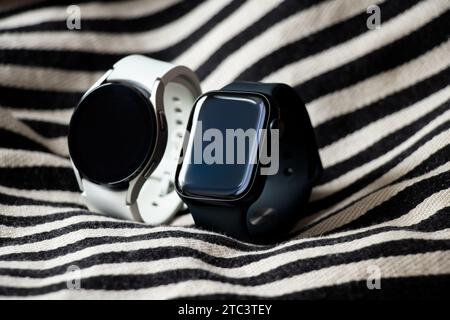 Dnipro, Ukraine - 10. Dezember 2023: Smart Uhren Samsung Galaxy Active Watch weiß und Apple Watch Series 8 schwarz liegen auf einem gestreiften schwarz-weißen F Stockfoto