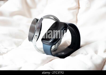 Dnipro, Ukraine - 10. Dezember 2023: Smart Uhren Samsung Galaxy Active Watch weiß und Apple Watch Series 8 schwarz liegen auf einem leichten Stoff, Smart Watch Stockfoto