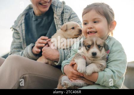 Junge Mutter und kleine süße Tochter, die Spaß beim Spielen mit Hunden im Freien haben. Glückliche Familie mit Haustierfreundschaft und Betreuungskonzept. Stockfoto