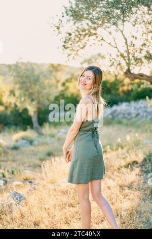 Lächelnde junge Frau steht im Garten um sich herum. Rückansicht Stockfoto