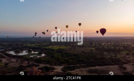 Ein atemberaubendes Bild einer Schar Heißluftballons, die über eine Landschaft mit üppigen Bäumen schweben und eine wunderschöne Himmelslandschaft schaffen Stockfoto