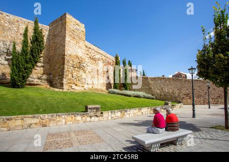 Ältere Ehepaare sitzen auf einer Steinbank unter den mittelalterlichen Stadtmauern in der spanischen Stadt Salamanca Spanien Stockfoto