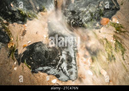 Nahaufnahme von bewegungsunscharfen Wasserstürmen, die über einen Cobble Stones fließen Stockfoto