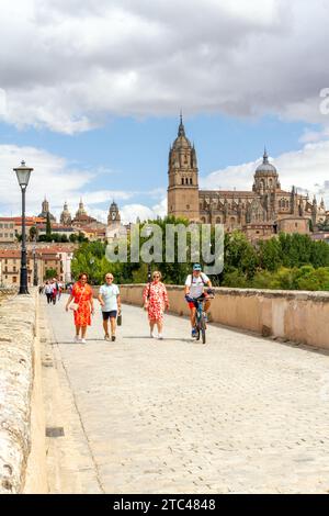 Menschen gehen über die mittelalterliche römische Brücke von Salamanca über den Fluss Tormes mit Blick auf die neue Kathedrale von Salamanca im Hintergrund Spanien Stockfoto