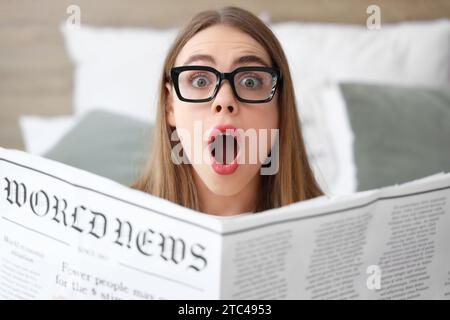 Eine schöne schockierte junge Frau, die zu Hause im Schlafzimmer Zeitung liest Stockfoto