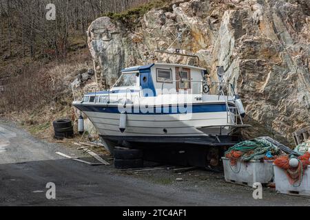 Lindesnes, Norwegen - 16. April 2022: Weißes und blaues Plastikfischboot an einer Straße. Stockfoto