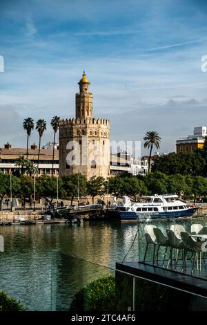 Der historische Torre del Oro steht hoch neben dem Fluss Guadalquivir mit Palmen und einem Boot in Sevilla., Spanien. Stockfoto