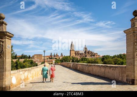 Menschen gehen über die mittelalterliche römische Brücke von Salamanca über den Fluss Tormes mit Blick auf die neue Kathedrale von Salamanca im Hintergrund Spanien Stockfoto