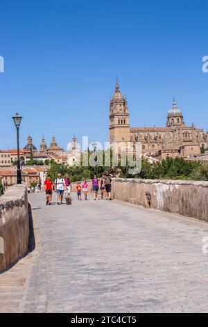 Menschen gehen über die mittelalterliche römische Brücke von Salamanca über den Fluss Tormes mit Blick auf die neue Kathedrale von Salamanca im Hintergrund Spanien Stockfoto