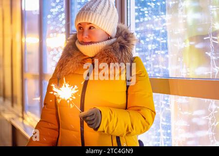 Eine junge Frau mit Strickmütze hält den Glitzer in den Händen. Glänzende Schaufenster auf dem Weihnachtsmarkt, Shopping und Verkauf. Stockfoto