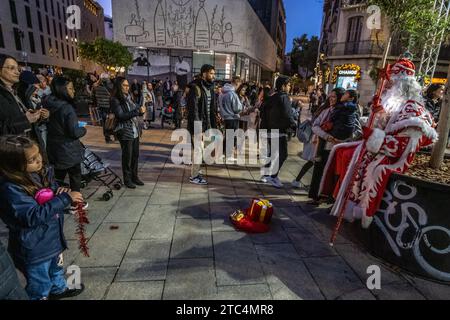 Barcelona, Spanien. Dezember 2023. Eine Gruppe von Menschen wird um einen Straßenkünstler, der als Zauberkönig verkleidet ist, auf der Esplanade der Kathedrale von Barcelona gesehen. Die Stadt Barcelona ist bereits in die Weihnachtszeit eingetaucht. Weihnachtsdekoration, Kunsthandwerksmessen und weihnachtliche Straßenbeleuchtung in Einkaufszentren fördern den Verkauf und die Unterhaltung von Familien. Quelle: SOPA Images Limited/Alamy Live News Stockfoto