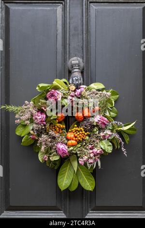 Ein Weihnachtskranz aus getrockneten roten Rosen, falschen Kürbissen, Dillzweigen, Samen, Lorbeerzweigen, getrocknete Äste, Eukalyptus und Pflanzen schmücken die Vorderseite Stockfoto