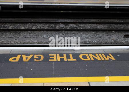 Gelb gemaltes Schild „Mind the Gap“ am Bahnsteigerrand des Bahnhofs aus nächster Nähe Stockfoto