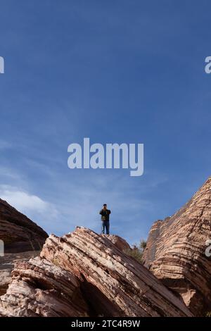 Ein Mann, der auf Felsen steht und ein Telefonfoto macht, im Red Rock Canyon in Nevada. Stockfoto