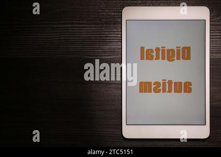 Tablet mit Phrase Digital Autism auf Holztisch, Draufsicht und Platz für Text. Suchtverhalten Stockfoto
