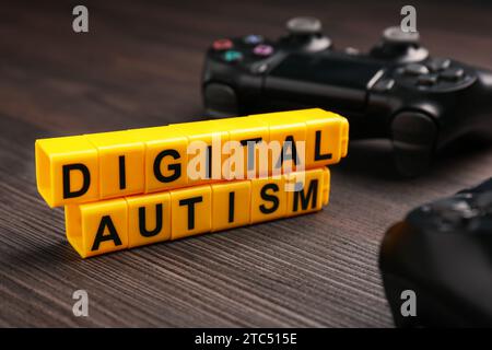 Phrase Digital Autismus aus gelben Würfeln und Gamepad auf Holztisch, Nahaufnahme. Suchtverhalten Stockfoto