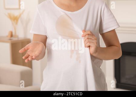 Frau zeigt Flecken von Kaffee auf ihrem Hemd drinnen, Nahaufnahme Stockfoto