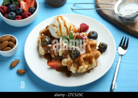 Köstliche belgische Waffeln mit Eis, Beeren und Karamellsauce auf hellblauem Holztisch, Nahaufnahme Stockfoto