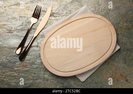 Schneidebrett aus Holz, Serviette und Besteck auf strukturiertem Tisch, flache Ladefläche. Leerzeichen für Text Stockfoto