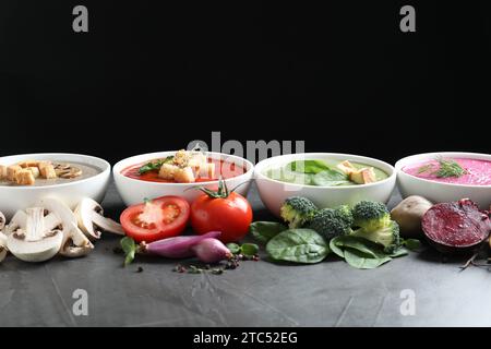 Verschiedene leckere Cremesuppen in Schüsseln und Zutaten auf dunkelgrauem Tisch Stockfoto