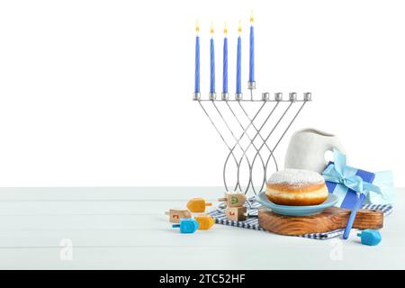 Hanukkah-Feier. Komposition mit Menora, Dreidels und Donut auf Tisch vor weißem Hintergrund Stockfoto