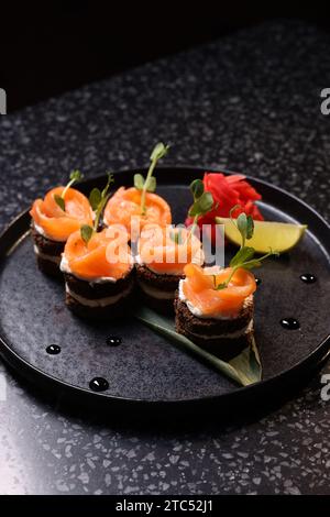 Leckere Canapes mit Lachs, Frischkäse und Mikrogrün auf dunklem Tisch Stockfoto