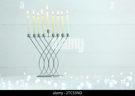 Hanukkah-Feier. Menora mit brennenden Kerzen und festlichen Lichtern auf dem Tisch vor hellem Hintergrund, Platz für Text Stockfoto