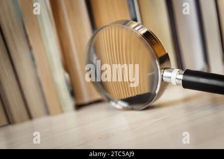 Bücher auf dem Tisch mit einem Fragment, das durch eine Lupe vergrößert wurde. Makrofotografie. Konzept der Forschung, Untersuchung und Suche nach Informationen Stockfoto